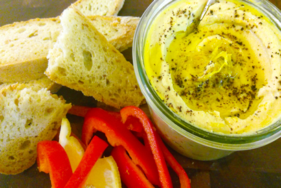 Silky Smooth Hummus topped with olive oil, lemon zest, and sumac, with bread and red peppers for dipping