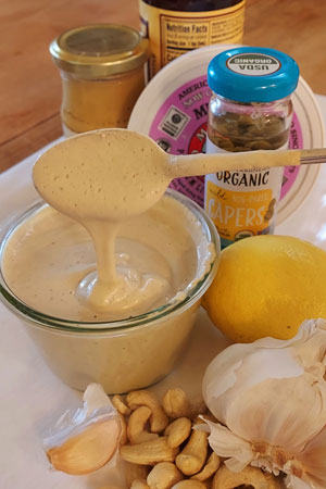 creamy vegan caesar dressing surrounded by ingredients - garlic, cashews, lemon, capers, miso, garlic, worcestershire